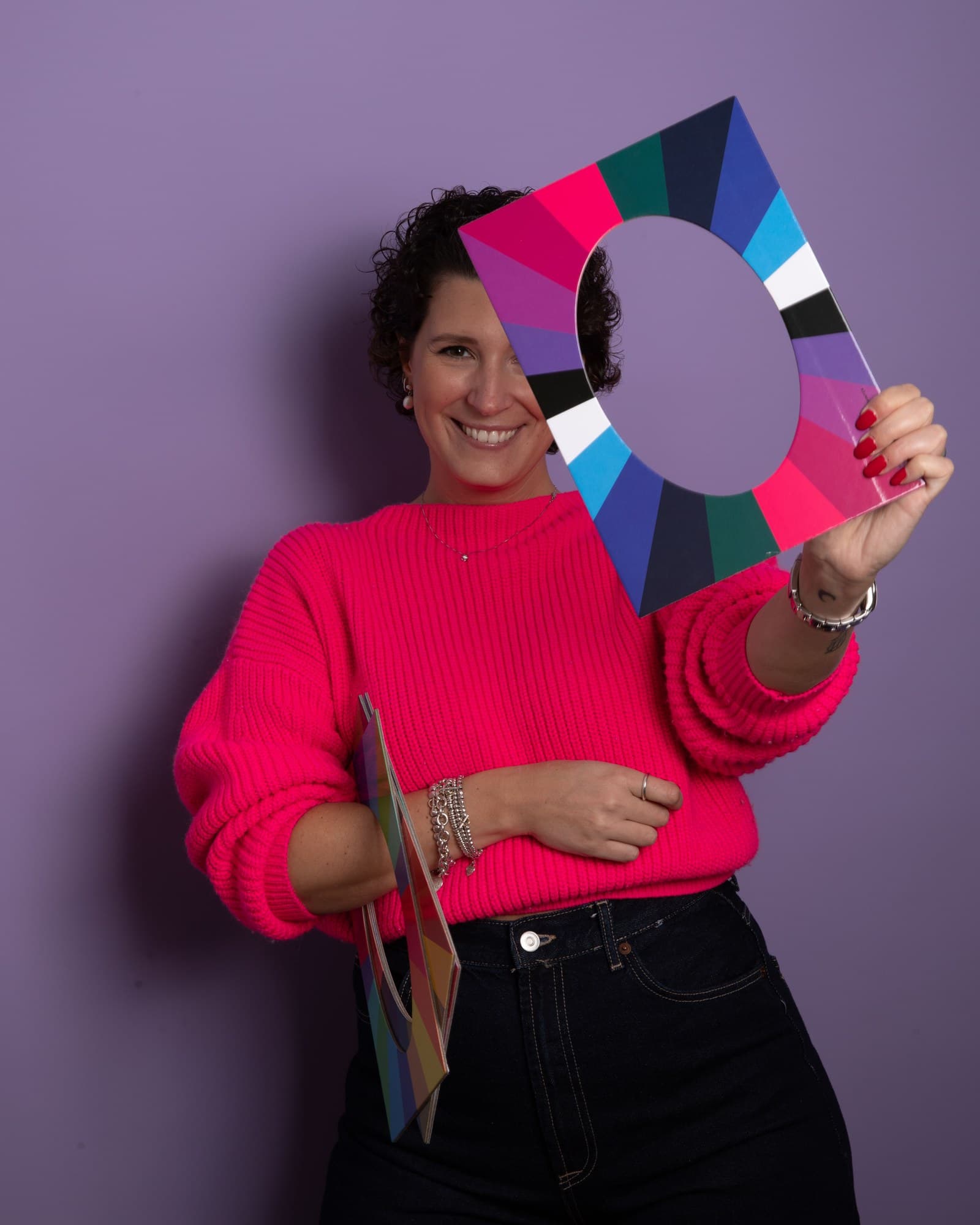 Camilla Petit, consultora de imagen CiPiCROMIE, con jersey rosa intenso, sostiene ante su rostro una carta cromática calada con los colores de su paleta, sobre fondo violeta